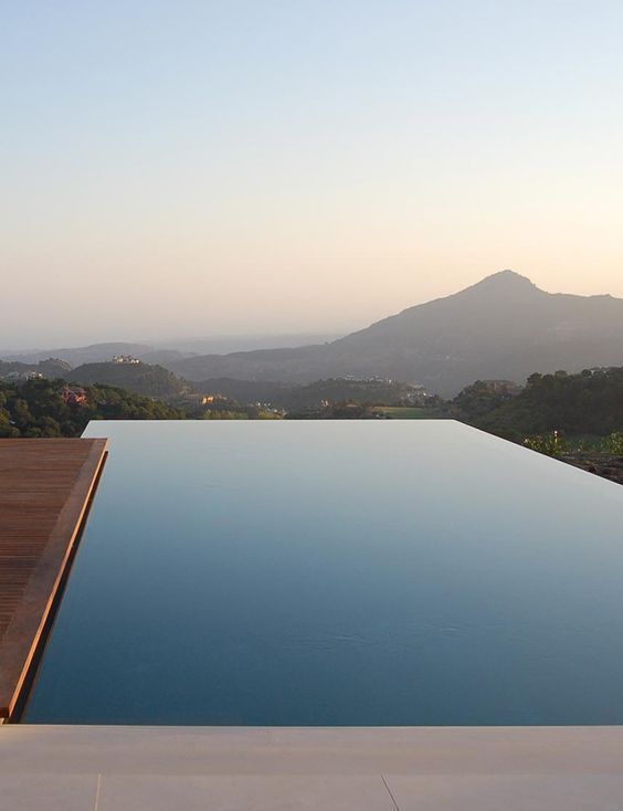 an infinity pool with a mountain view and a wooden deck compose a lovely minimalist outdoor space to have a rest in