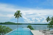 an infinity pool with a stone deck and steps, with a sea view and greenery and trees is a fantastic space to have a rest in