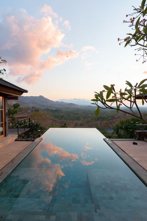 an infinity pool with a view of the woodlands and mountains and a stone deck plus greenery around is amazing