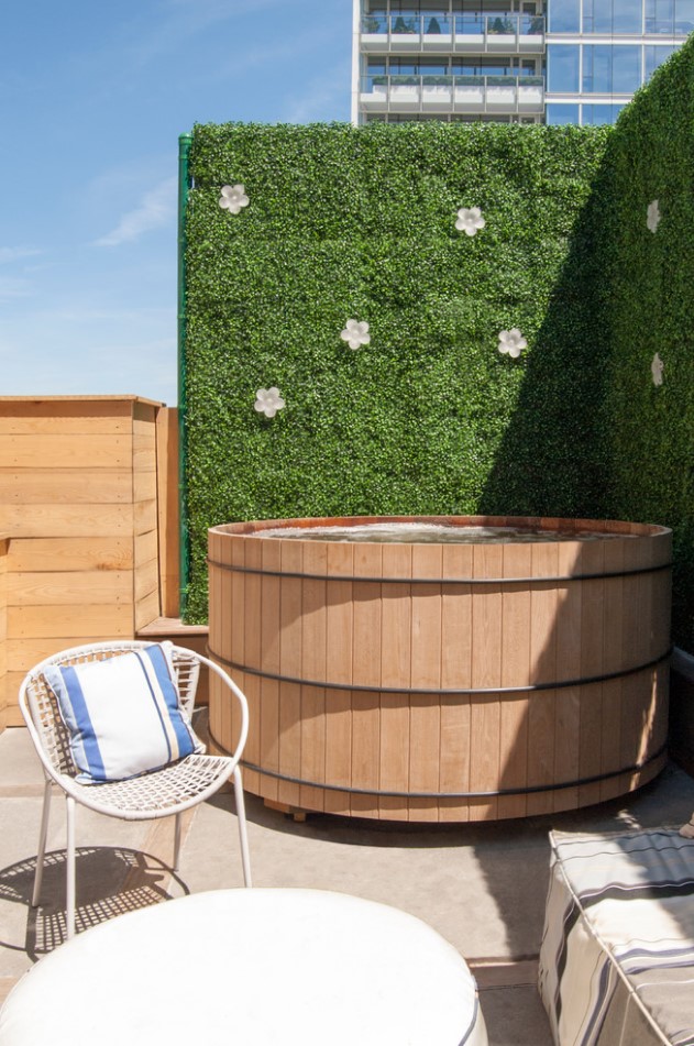 an outdoor space with a hot tub of wood, a living wall as a privacy screen, modern white outdoor furniture and striped upholstery