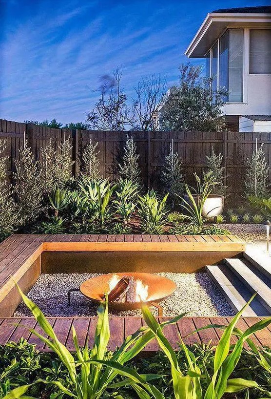 an outdoor sunken fire pit with gravel around and a deck that doubles as a bench around the pit is a cool modern solution