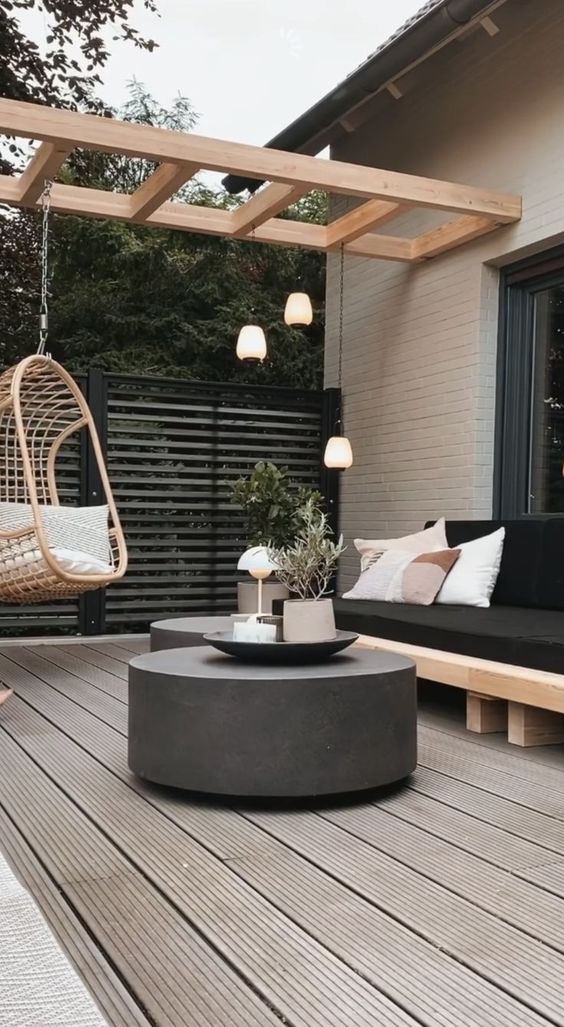 a Scandi terrace with a black sofa, a pendant rattan chair, a duo of dark concrete tables and pendant lamps