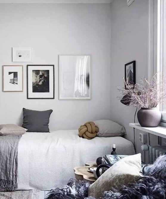 a Scandinavian bedroom with a bed with grey bedding, a nightstand with hairpin legs, a gallery wall and an additional art