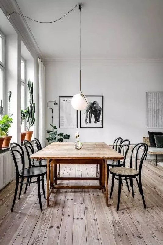 a Scandinavian dining space with a stained table and black chairs, a mini gallery wall, potted plants and a pendant lamp
