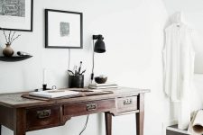 a Scandinavian home office with a dark-stained desk and a black stool, a mini gallery wall and a black sconce
