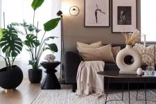 a Scandinavian living room with taupe and greige walls, black furniture, potted plants and a mini black and white gallery wall