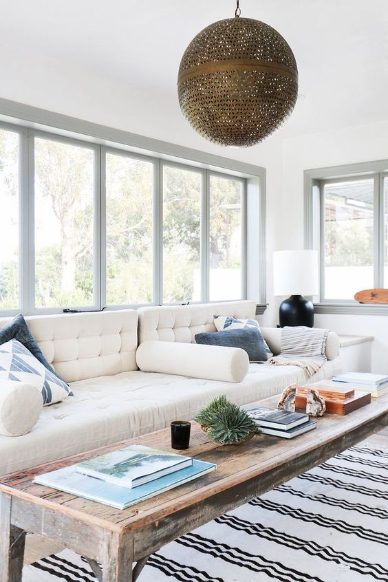 a Scandinavian sunroom with a creamy sofa, a stained coffee table, a striped rug and a sphere pendant lamp and some table lamps