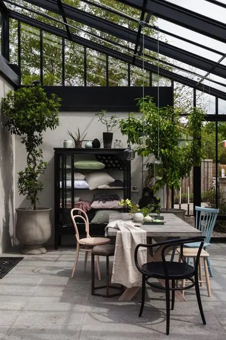 a Scandinavian sunroom with mismatching chairs, a wooden table and a large storage unit, potted greenery