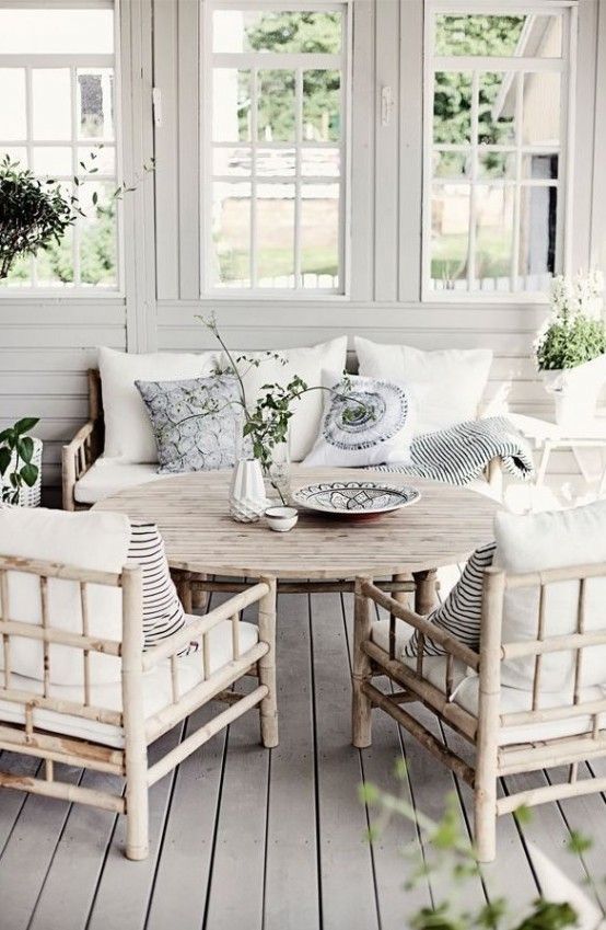 a Scandinavian sunroom with rattan furniture, with neutral upholstery, potted greenery and printed pillows is peaceful and welcoming