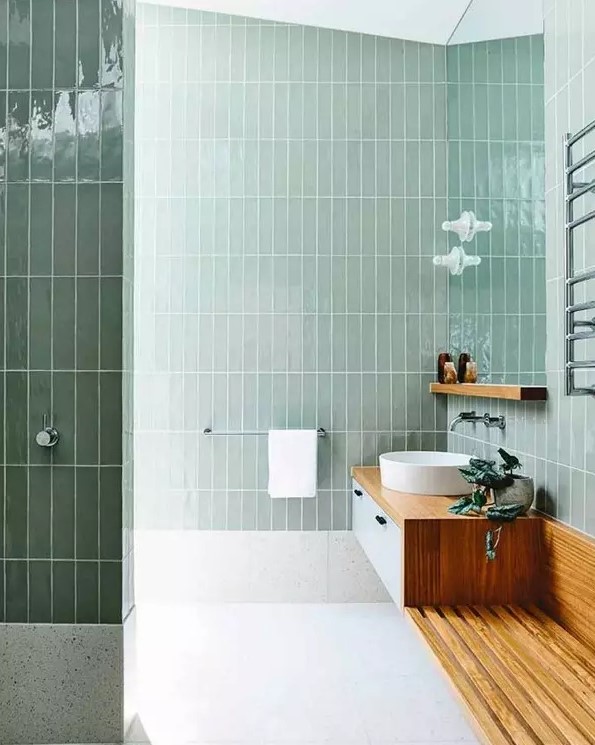 a bathroom clad with mint skinny stacked tiles, white terrazzo tiles on the floor, a floating vanity with a built-in bench
