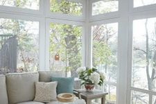 a beach sunroom with neutral furniture, a woven table, blooms and greenery and a cool beach view