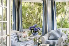 a beach sunroom with white wicker furniture and blue striped upholstery plus a vintage blue table and blue curtains