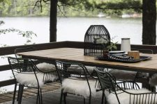 a beautiful Scandinavian dining space with a light-stained dining table, black metal chairs with faux fur, a lovely lake view