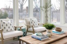 a beautiful and airy Scandinavian sunroom with a duo of coffee tables, neutral chairs, potted greenery and side tables