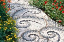 a beautiful and chic pebble garden path with white and grey swirl patterns and bright blooms along the path is wow