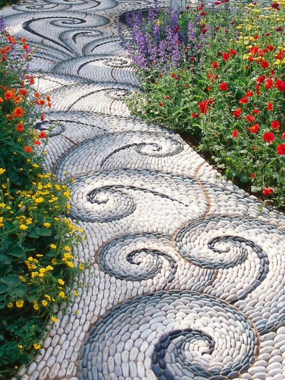 a beautiful and chic pebble garden path with white and grey swirl patterns and bright blooms along the path is wow