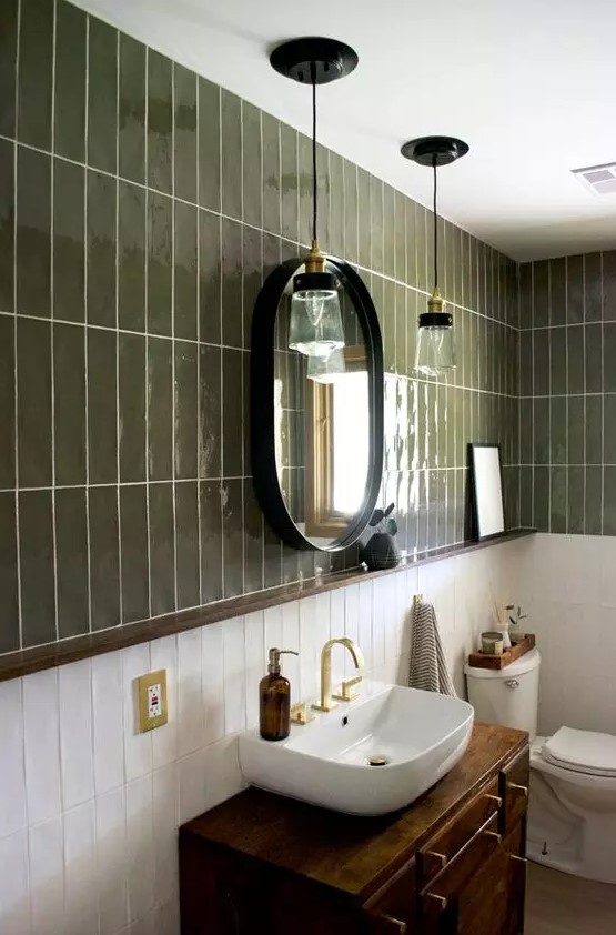 a beautiful and elegant bathroom with green and white stacked tiles, a dark-stained vanity with a sink, an oval mirror and pendant lamps