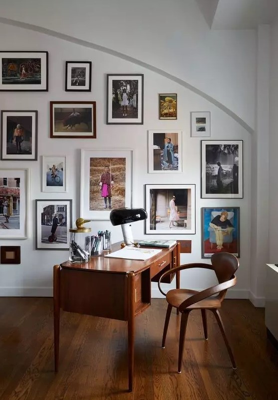 a beautiful and refined home office with a rich stained desk and a chair, a colorful gallery wall on an arched wall
