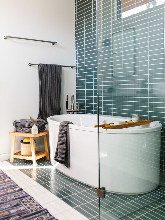 a beautiful contemporary bathroom with turquoise stacked tiles, an oval tub, a bold rug and graphite grey textiles
