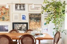 a beautiful eclectic dining room with a stained table and vintage chairs, a potted tree and a free form gallery wall with much color