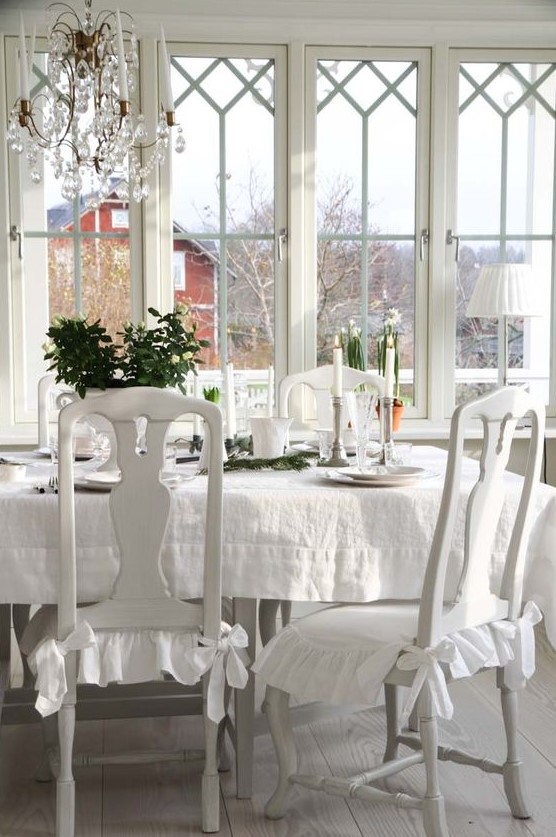 a beautiful vintage sunroom in white, vintage furniture, a crystal chandelier, candles and potted plants