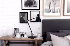 a black and white bedroom with a black upholstered bed, monochromatic bedding, a stained nightstand, a cool gallery wall