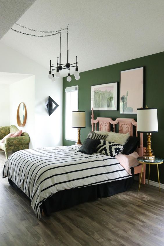 a boho bedroom with white walls and a green accent one, bold printed bedding, a mini gallery wall with cacti and a chic chandelier