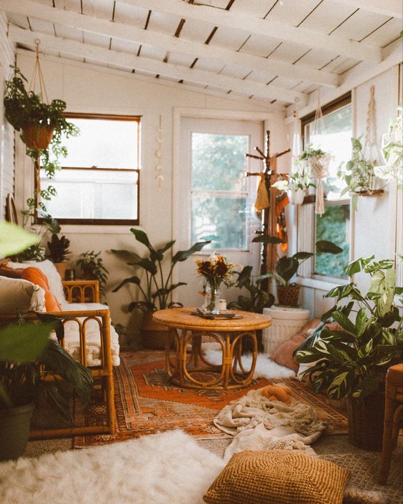 a boho sunroom with rattan furniture, a bold rug and lots of pillows on the floor, potted plants is a very welcomign and warm space