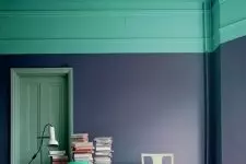 a bold home office with violet walls, a mint green ceiling, a desk and a mint chair and stacks of books