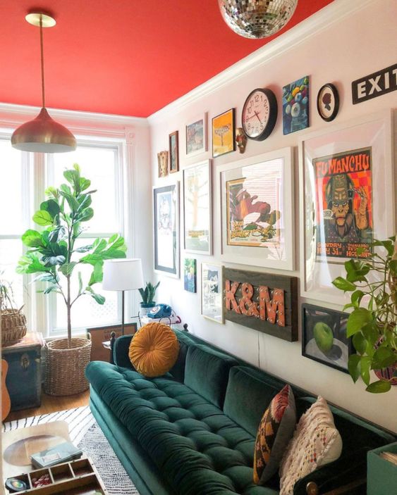 a bold living room with a hot red ceiling, a dark green sofa with pillows, a bold and catchy gallery wall and pendant lamps
