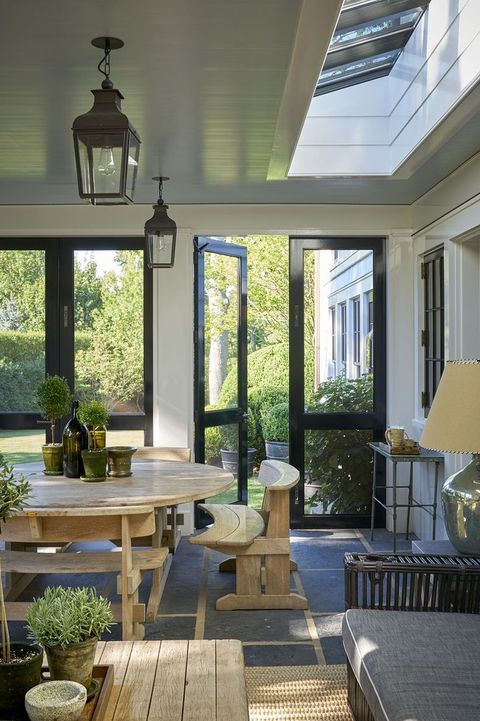a breezy modern farmhouse sunroom with a light-stained dinign set, a console and some outdoor lantenrs, a grey sofa and benches