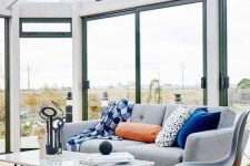 a bright Scandi sunroom with a grey sofa, a chair and a coffee table, bright pillows and a view is great and light-filled