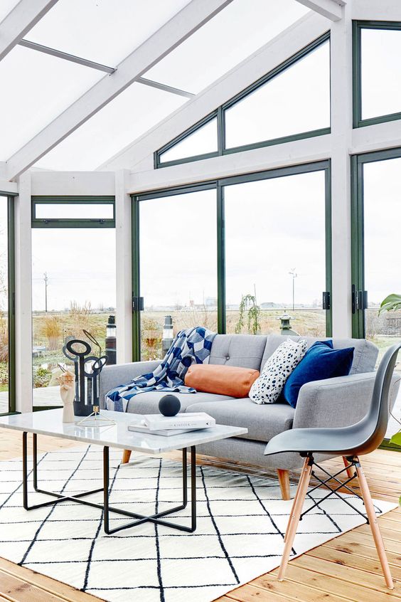 a bright Scandi sunroom with a grey sofa, a chair and a coffee table, bright pillows and a view is great and light-filled
