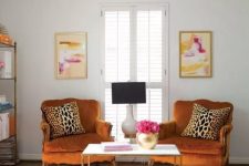 a bright and chic space with rust-colored vintage chairs, a pink printed rug, a storage unit and bold artworks