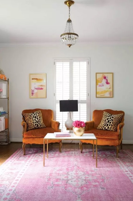 a bright and chic space with rust colored vintage chairs, a pink printed rug, a storage unit and bold artworks