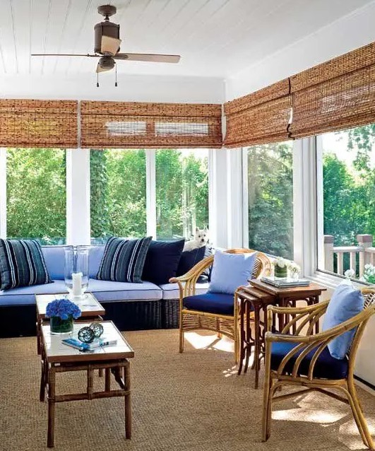 a bright beach sunroom with a rattan furniture, bright blue and navy upholstery and bamboo tables and shades