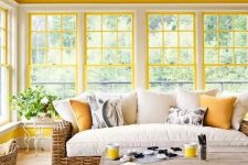 a bright farmhouse sunroom with sunny yellow window framing, wicker furniture, a vintage chandelier is very welcoming