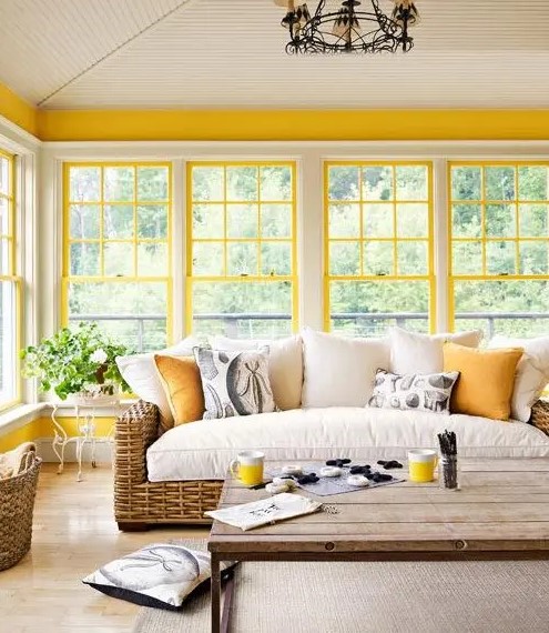 a bright farmhouse sunroom with sunny yellow window framing, wicker furniture, a vintage chandelier is very welcoming