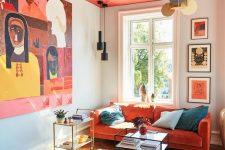 a bright living room with a hot red ceiling, an orange sofa, a navy chair, a bold artwork and pendant lamps plus elegant coffee tables