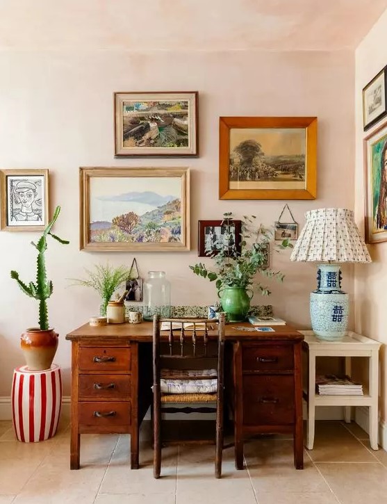 a bright mid century modern home office with blush walls, a stained desk and a chair, a colorful gallery wall and greenery and a cactus