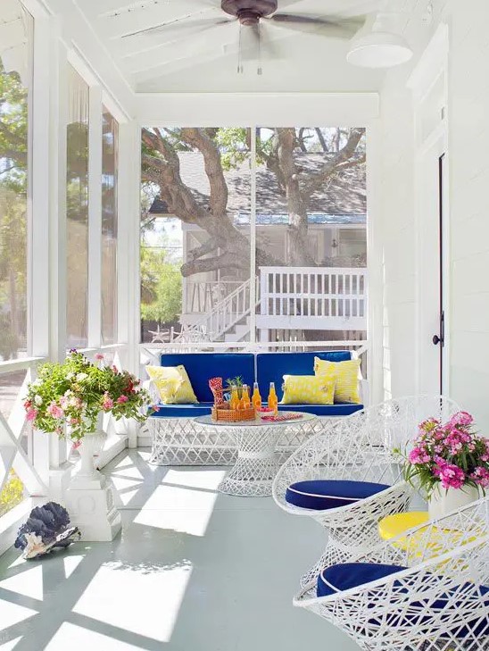 a bright modern beachy sunroom with white metal furniture with super bold upholstery, some potted blooms and seashells