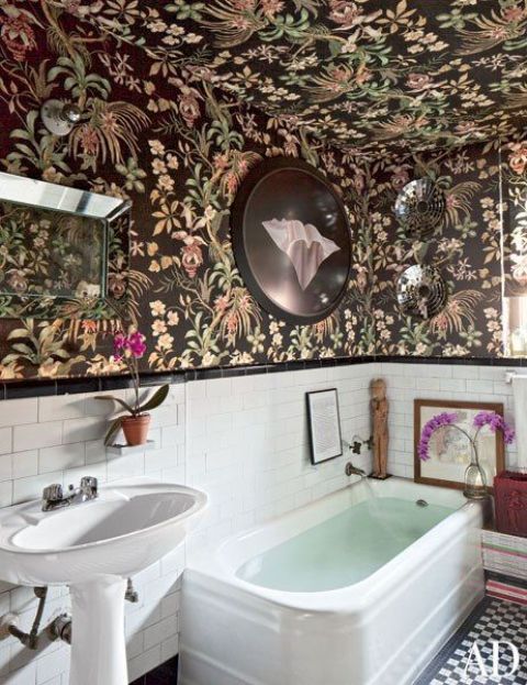 a catchy bathroom with dark wallpaper on the walls and ceiling, white subway tiles and a tub, a free standing sink and some art