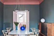 a catchy dining room with navy walls, a pink ceiling, a dining table, neutral chairs, pendant lamps and a color block credenza