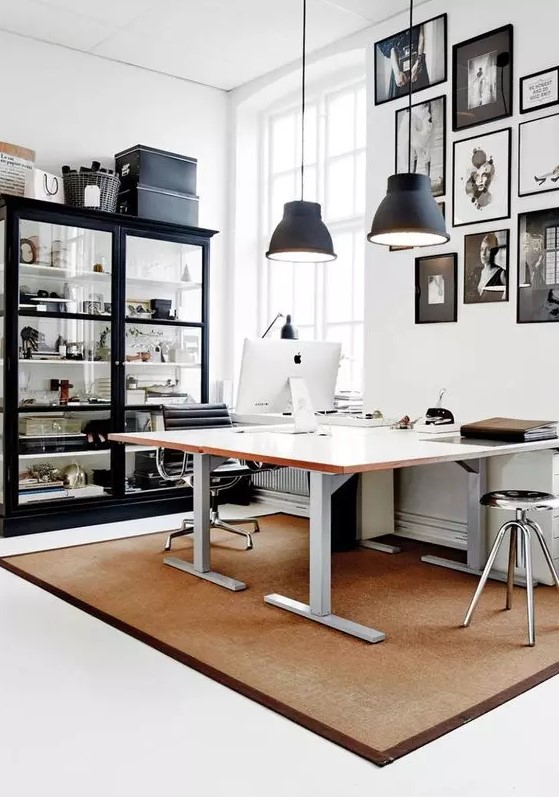 a chic Scandinavian home office with a shared desk, a large glass storage unit, a gallery wall in black and white and black pendant lamps