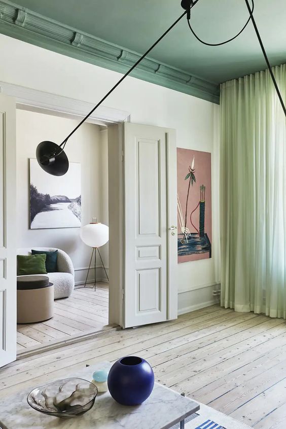 a chic Scandinavian home with neutral walls,a  bold green ceiling, light green curtains, a coffee table and a navy vase