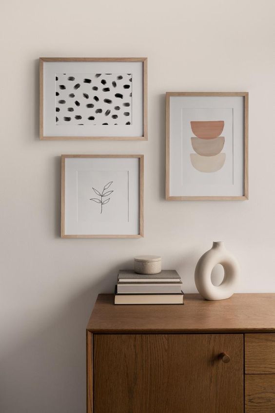 a chic and serene space with a stained credenza, a peaceful and soothing mini gallery wall of prints, a vase and books