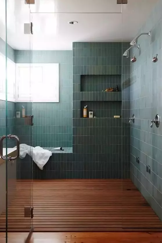 a chic bathroom with a large shower space clad with green stacked tiles, with a bench and niches in the walls, a dark-stained floor and windows for natural light