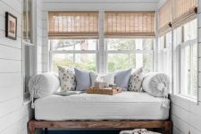 a chic country house sunroom with a daybed with a mattress and pillows, shades and a bread bowl is welcoming