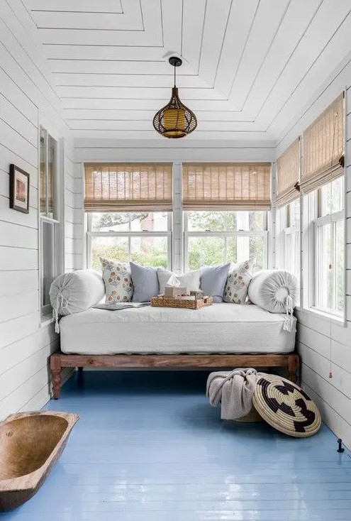 a chic country house sunroom with a daybed with a mattress and pillows, shades and a bread bowl is welcoming