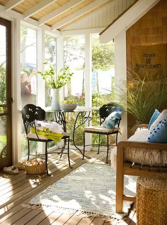 a chic eclectic sunroom space with forged chairs and a table and a wooden benches with textiles and accessories